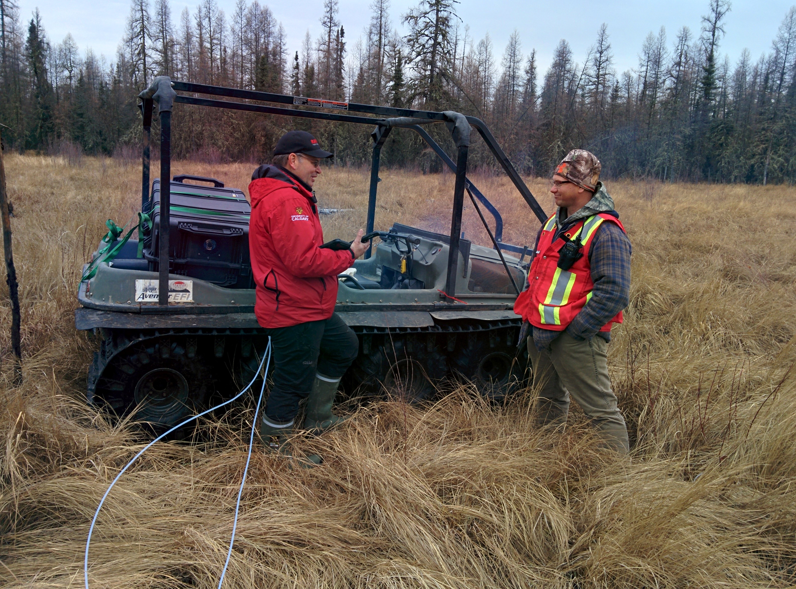 Deux chercheurs se tiennent debout à côté du véhicule Argo, à bord duquel a été installée la technologie de détection des fuites atmosphériques, dans un milieu humide gazonné à Christina Lake, en Alberta.   